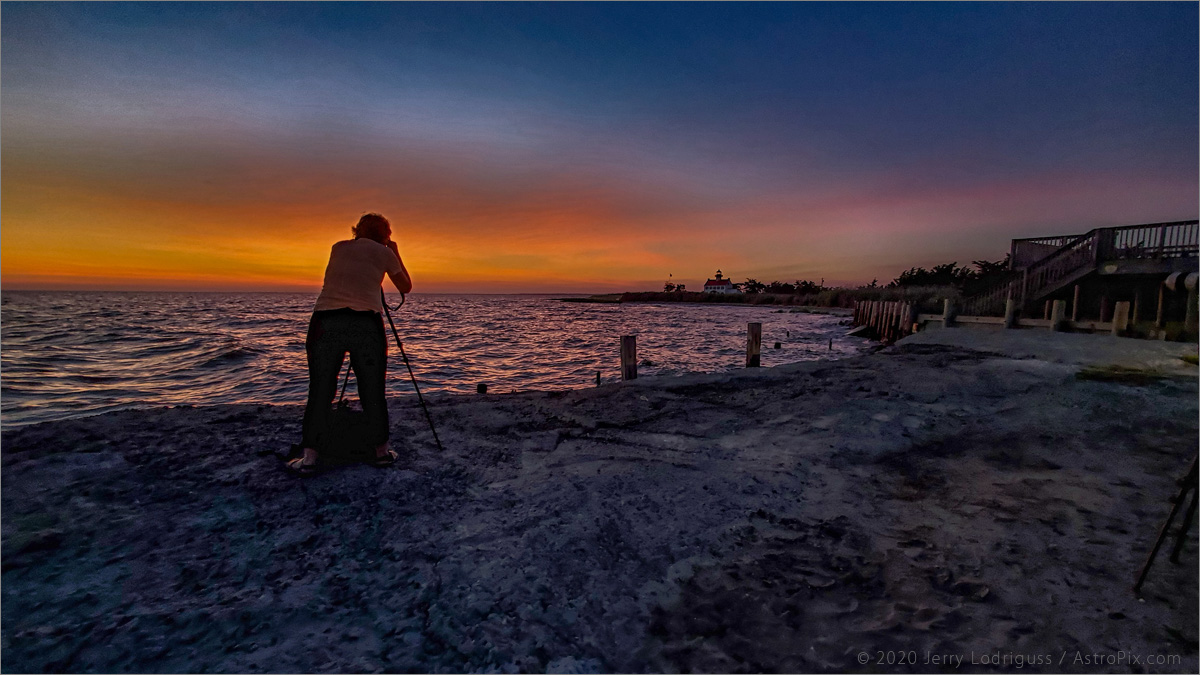 A photographer shoots sunset clouds and East Point Lighthouse.<br /><br />Galaxy S10 cell phone<br />1.8mm focal length lens<br />1/30th second exposure at ISO 160 at f/2.2