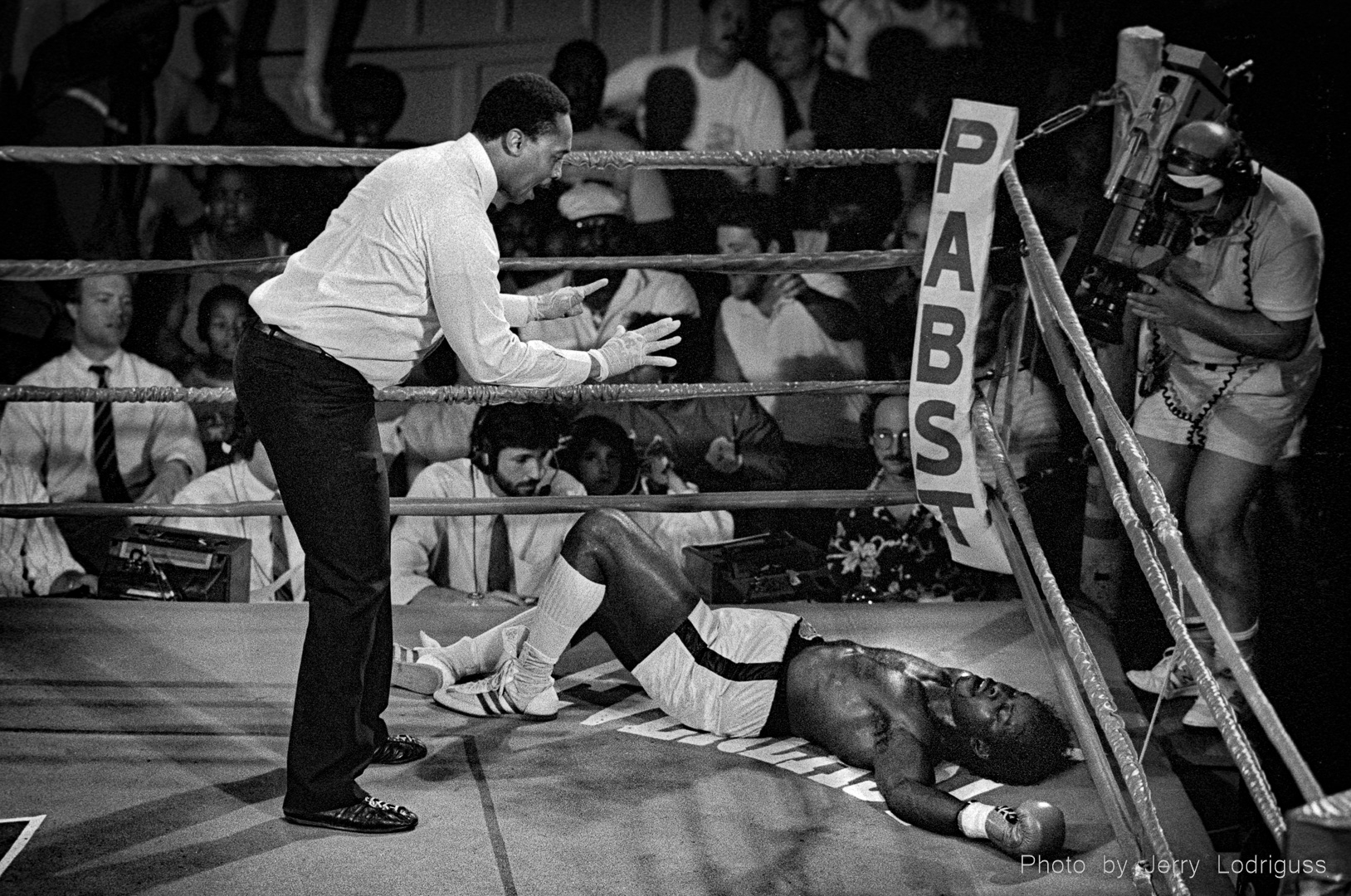 A boxer is knocked out, down on his back on the canvas in the ring, as the referee counts him out.
