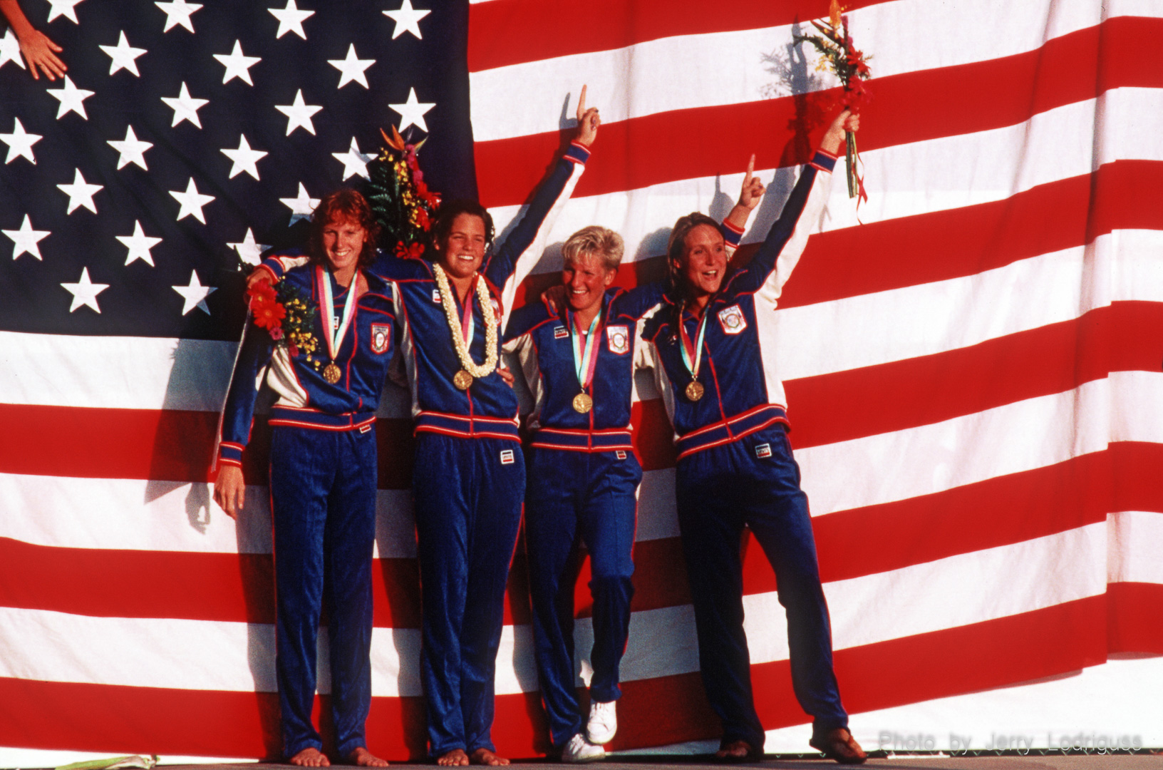 Teammates in the USA women's 4 x 100 meter relay stop in front of a giant American flag to wave to fans after winning the gold medal and setting a world record in the finals of the event during the 1984 Olympics in Los Angeles.