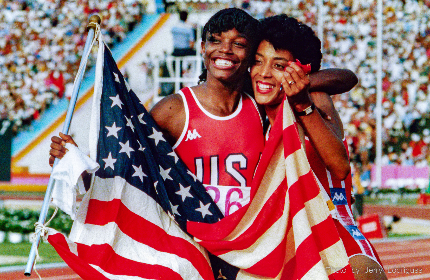 Smiling and laughing, Valerie Brisco-Hooks (left), winner of the gold medal in the 200 meter dash, and teammate Florence Griffith, winner of the silver medal, hold the American flag after the race. The victory gave Brisco-Hooks her second gold medal of the 1984 Olympic Games in Los Angles.